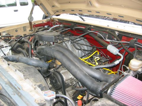 1990 Ford Bronco - The engine bay of a vehicle is shown, with various hoses, wires, and engine components visible.