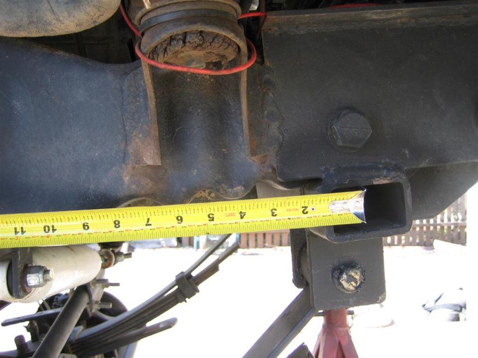 Measuring tape on vehicle frame near suspension components. Supermotors.net logo visible