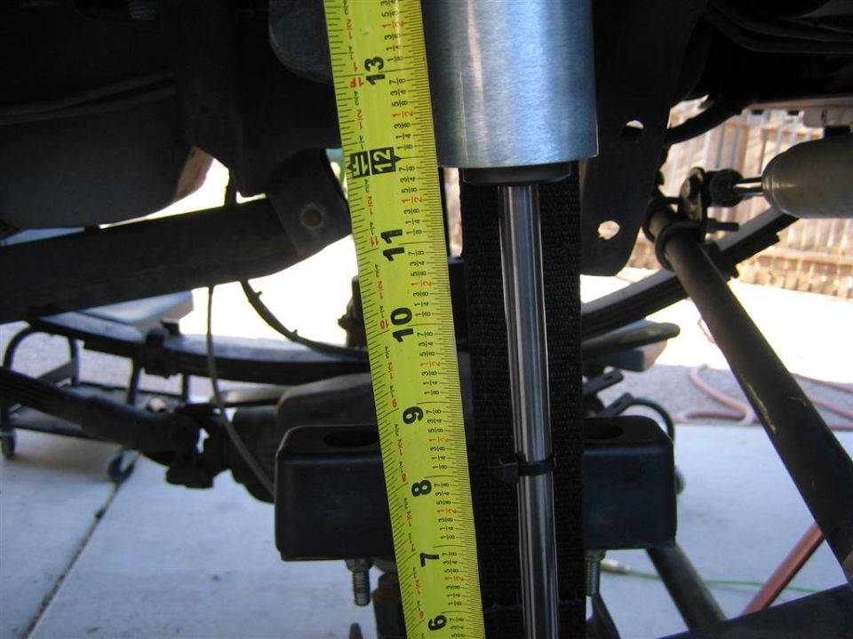 Measuring a shock absorber with a yellow tape measure. The tape shows about 11.5 inches
