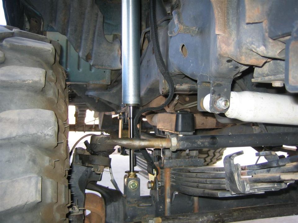 Close-up of a large tire and suspension components, including a shock absorber and leaf springs
