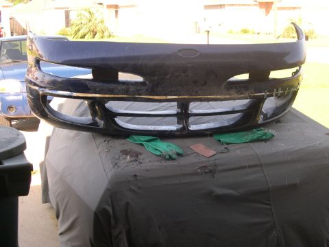 1997 Ford Probe - A car bumper is shown, with a blue vehicle partially visible behind it.