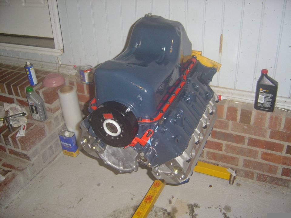 Blue-gray V8 short block upside down on a garage floor with oil pan and flexplate