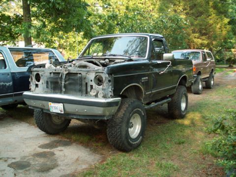 1988 Ford Bronco - Two SUVs are parked outdoors, one with its hood up, showing the engine bay.