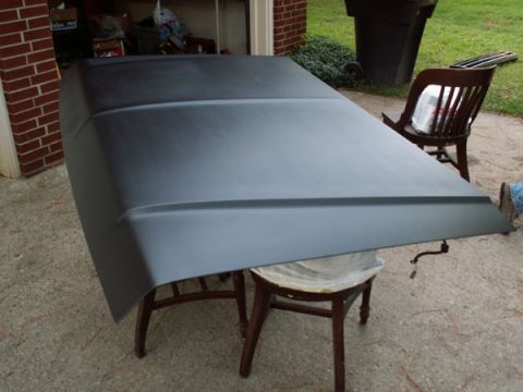 1988 Ford Bronco - A car hood is resting on two chairs outside, showing a primer finish and some attached wiring.