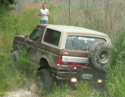 1988 Ford Bronco - A brown 1988 Ford Bronco navigates a grassy, off-road trail with a spare tire mounted on the back.