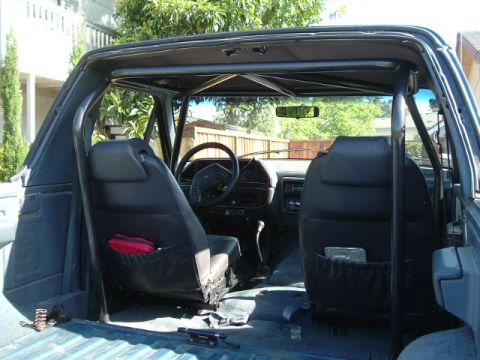 1989 Ford Bronco - The interior of a 1989 Ford Bronco shows its roll cage and front seats, with a first aid kit visible.