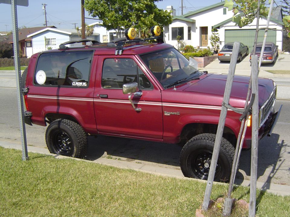Red 1985 Ford Bronco II with roof rack and off-road tires parked curbside