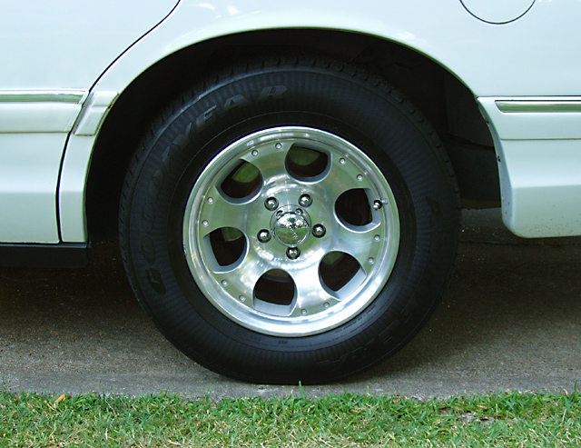 Close-up of a polished alloy wheel and Goodyear tire on a white sedan's rear fender