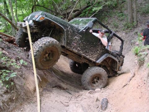 1992 Ford Bronco - A Jeep Wrangler navigates a challenging off-road course, with one wheel lifted high.