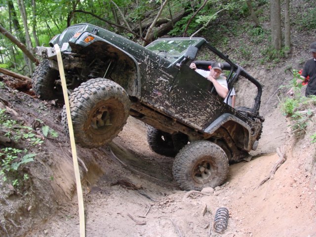 Green Jeep Wrangler climbing a steep, muddy trail with a driver inside