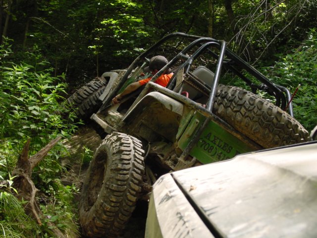 Off-road buggy with large tires climbing a steep, wooded trail