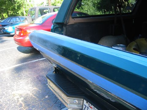 1996 Ford Bronco - Close-up along the open tailgate of a teal Ford Bronco, with the rear glass raised and the cargo area visible holding a paint can and yello…