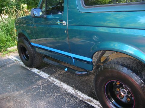 1996 Ford Bronco - Driver's side of a teal-green full-size Ford Bronco with blue masking tape running along the rocker and lower door line in preparation for…