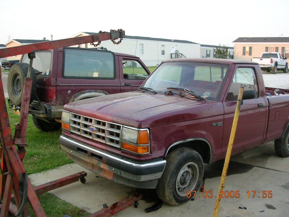 Maroon Ford Ranger on a trailer behind a tow rig, mobile homes in background