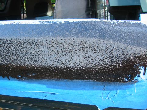 1996 Ford Bronco - Close-up of a body panel being roll-coated in black textured bedliner, the fresh coating still wet and heavily stippled. Blue painter's tap…