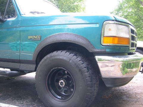 1996 Ford Bronco - Front three-quarter close-up of a teal Ford Bronco XL front fender with black textured bedliner coating rolled onto the wheel arch and lowe…