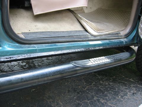 1996 Ford Bronco - Low close-up of a teal Ford Bronco door sill with the door open, showing fresh black textured bedliner coating applied to the rocker panel…
