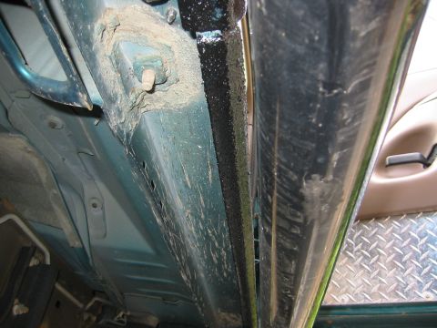 1996 Ford Bronco - Tight low-angle shot looking down the underside of a teal Ford Bronco between the body and a chrome tube side step, showing black textured…