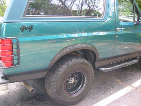1996 Ford Bronco - Rear three-quarter close-up of a teal Ford Bronco showing black textured bedliner coating on the rear wheel arch, lower quarter panel and r…