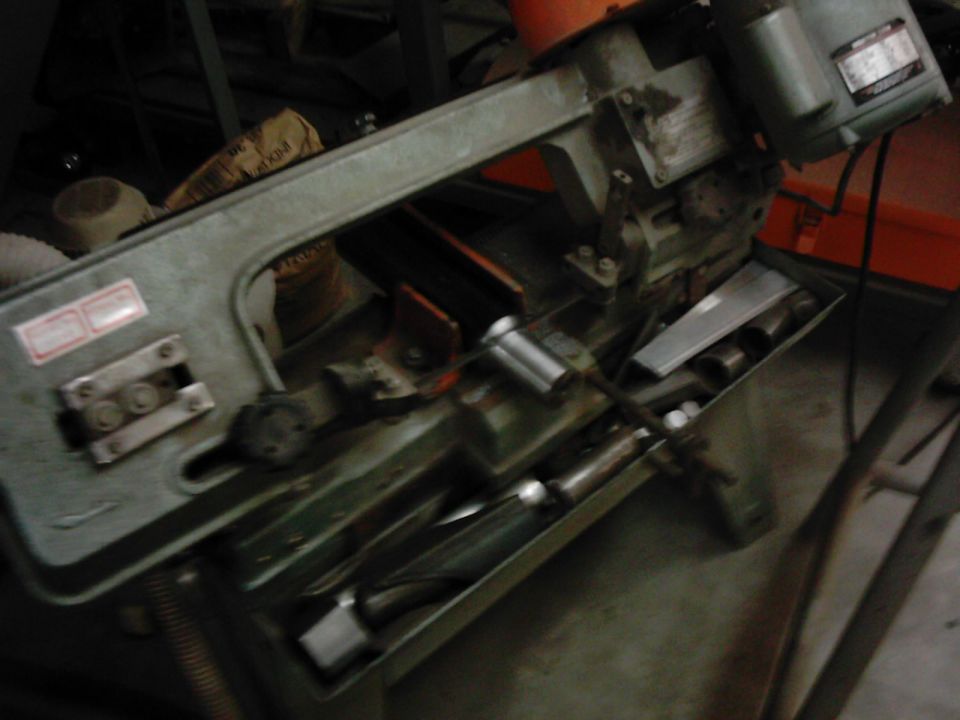 Green metal band saw with orange motor housing and a tray of metal parts