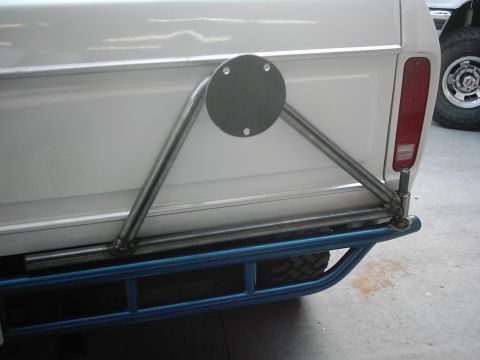 1978 Ford Bronco - Triangular tubular spare-tire carrier mounted to a white truck tailgate with a tube rear bumper.