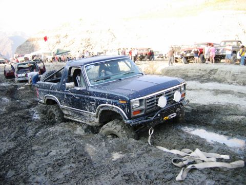 1985 Ford Bronco - Multiple vehicles are stuck in thick mud during an off-road event.