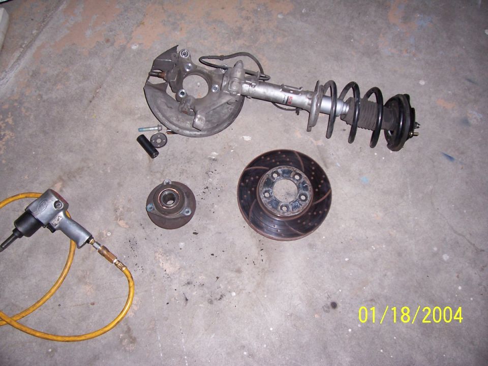 Disassembled car suspension components and an impact wrench on a concrete floor
