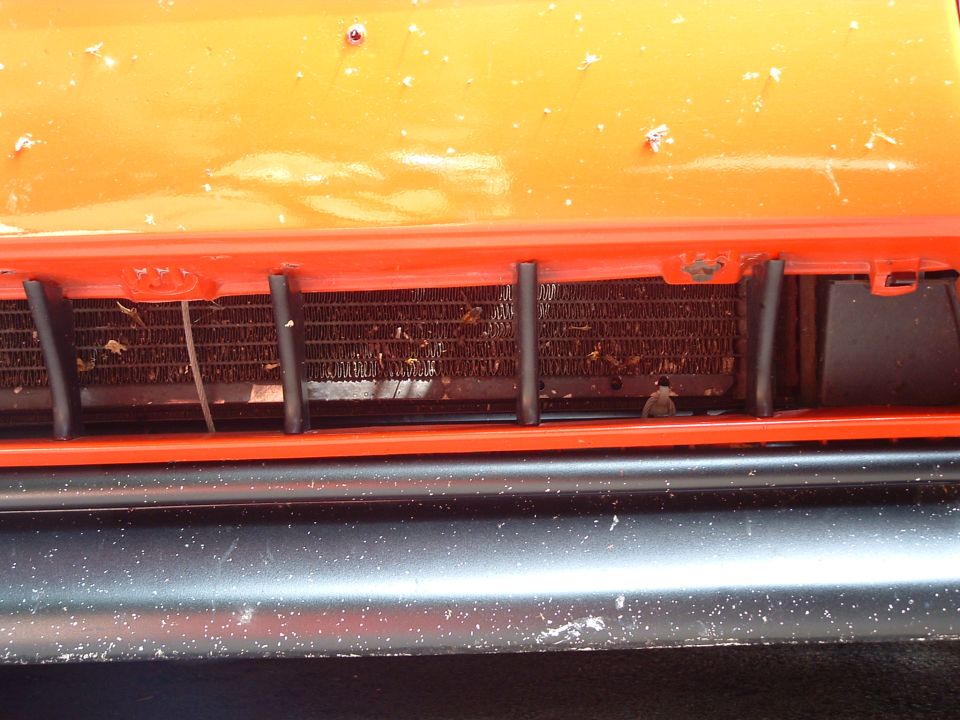 Close-up of car's orange hood, red grille, and radiator with debris