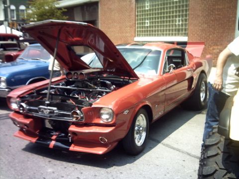 1995 Ford Probe - A red 1965 Ford Mustang coupe with its hood open is parked next to a blue car, displaying its engine and racing stripes.