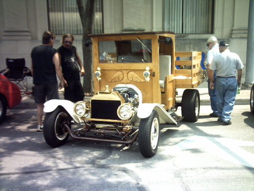 Wooden hot rod truck with exposed engine and white fenders. People stand around it