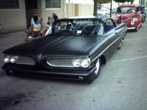 1995 Ford Probe - A line of vintage cars, including a matte black 1959 Pontiac Bonneville, are parked on a street.