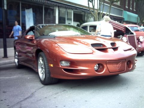 1995 Ford Probe - A copper-colored sports car is parked on a street, with other vehicles and buildings in the background.