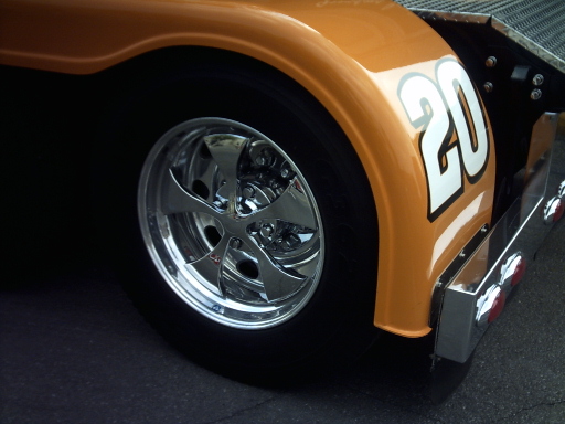 Orange race car rear fender with white number 20, chrome wheel, and tire. Supermotors.net logo visible