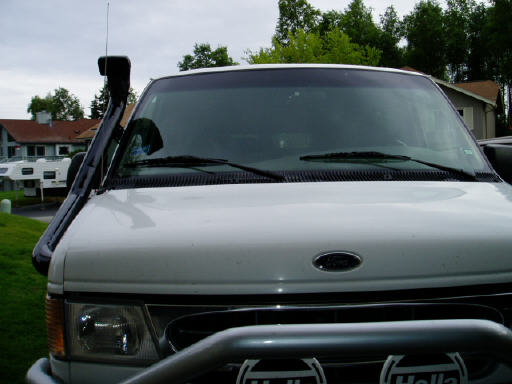 Front of white Ford van with snorkel beside windshield, RV in background