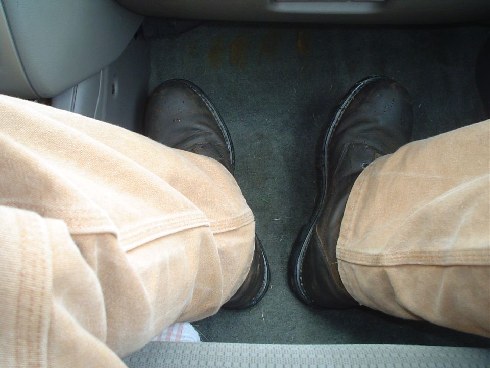 Driver's feet in brown boots and tan pants, visible on the floor mat inside a vehicle