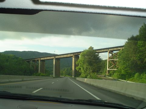 1981 Ford Bronco - Driving on a highway under a large railroad bridge with concrete pillars and a metal truss structure.