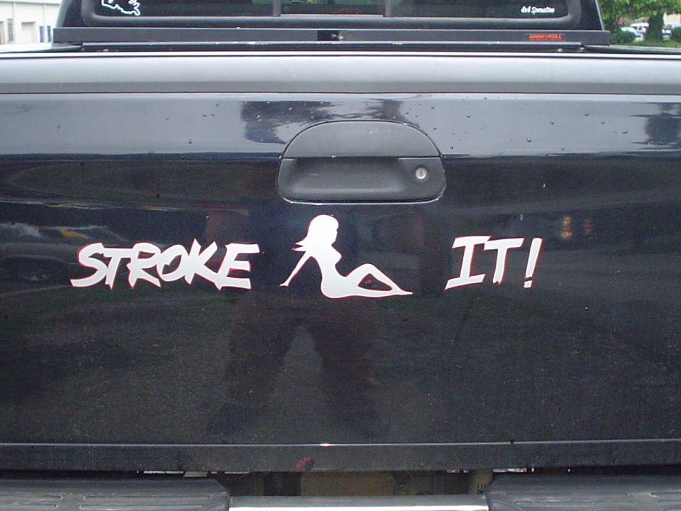Black truck tailgate with white sticker that says "STROKE IT!" and a silhouette of a woman