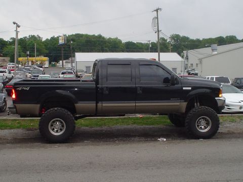 1981 Ford Bronco - A lifted black pickup truck is shown from the side, parked on a street with other vehicles in the background.
