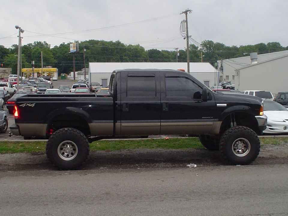 Lifted black pickup truck with tan lower body, 4x4 badging on the bed, parked on a street