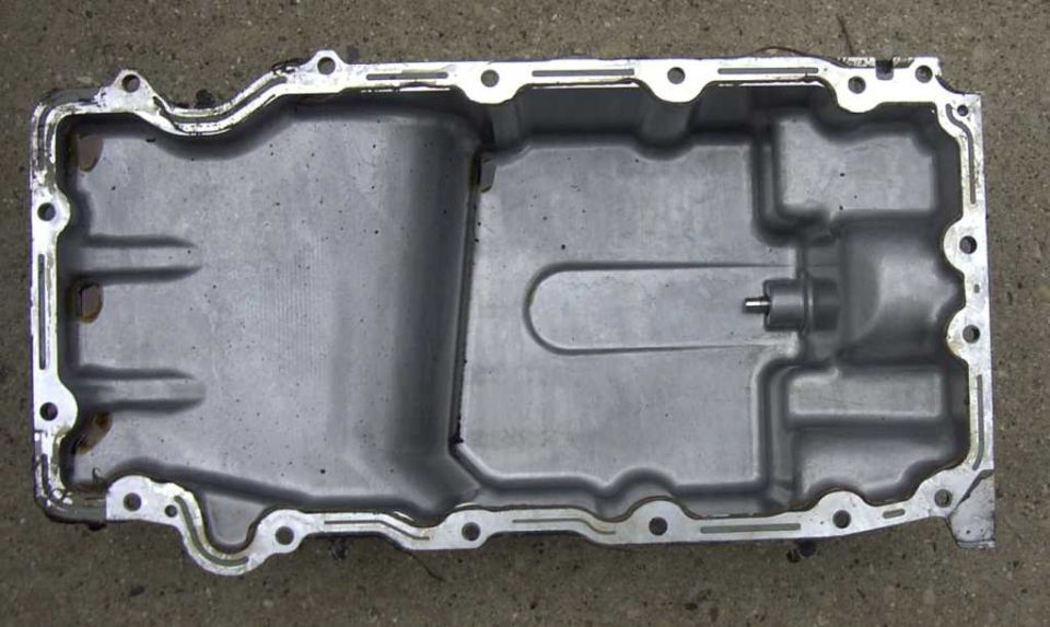 Aluminum engine oil pan sitting upside down on pavement