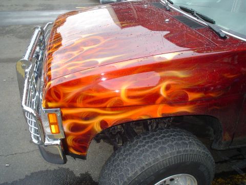 1981 Ford Bronco - This truck features a custom flame paint job on its hood and fender, with a chrome bumper and grille.