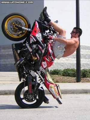 1994 Ford Bronco - A rider performs a wheelie on a red and black motorcycle on a paved surface.