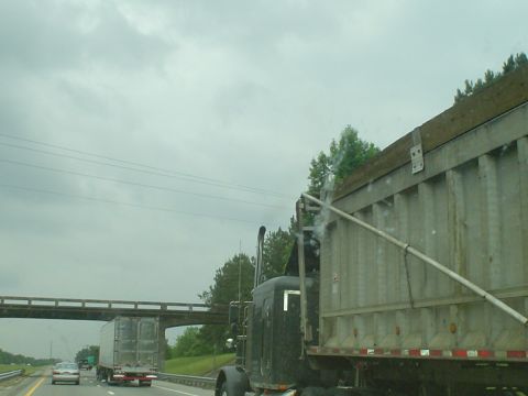 1981 Ford Bronco - A dump truck is seen from the side on a highway under a cloudy sky, with other vehicles in the distance.