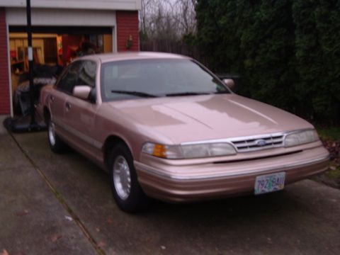 1996 Ford Crown Victoria LTD - This rose gold sedan is parked in front of a garage with a tree line in the background.