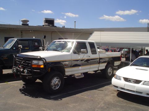 1981 Ford Bronco - A white Ford F-250 truck is parked next to other vehicles under a covered area.