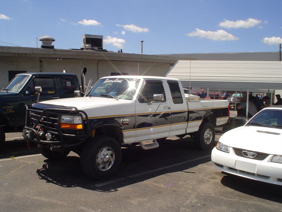 White Ford F-250 truck with black and gold stripes, bull bar, and dual exhaust pipes