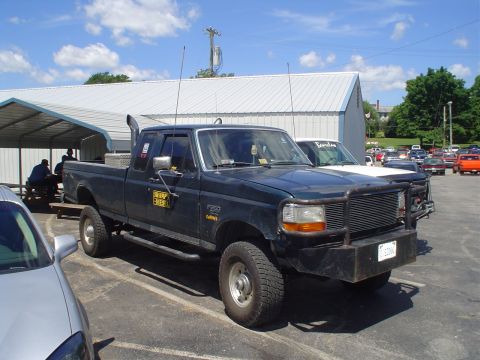 1981 Ford Bronco - A dark green Ford F-250 pickup truck is parked in a lot next to another vehicle, with a building in the background.