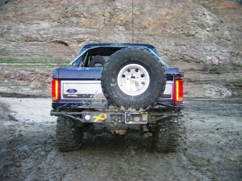1985 Ford Bronco - Rear view of a blue 1985 Ford Bronco, equipped with a spare tire on the tailgate and off-road modifications.