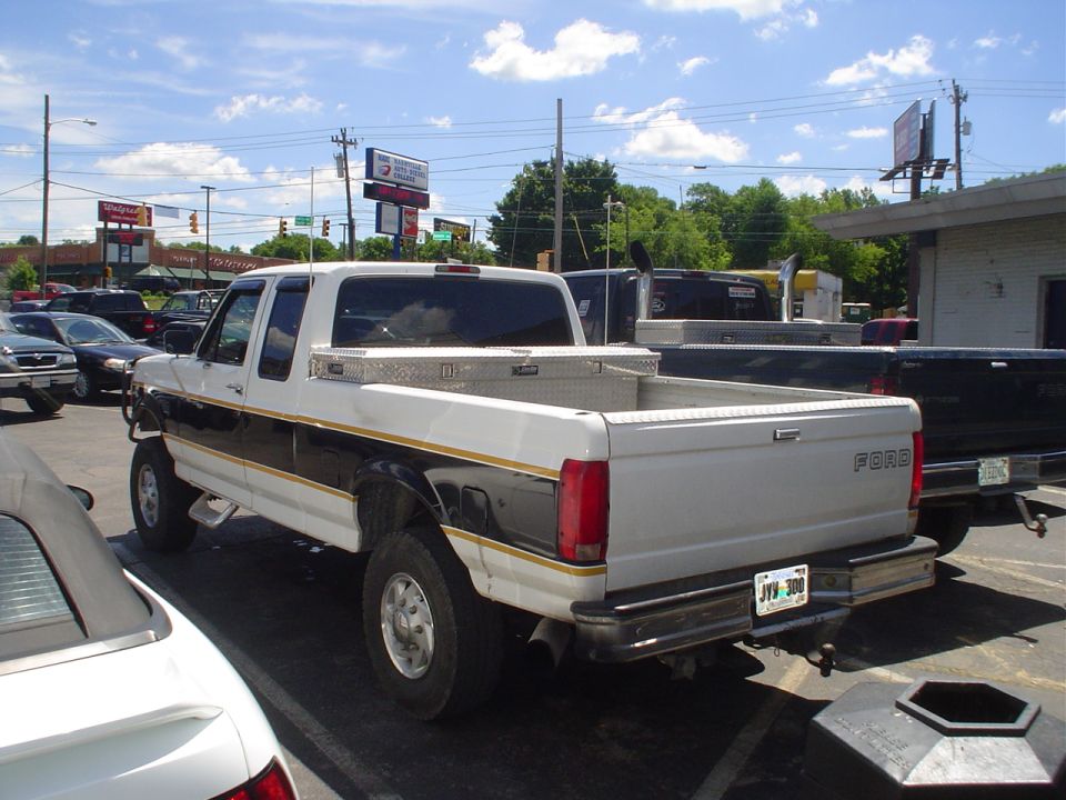 White Ford pickup truck with a toolbox in the bed, parked next to other vehicles