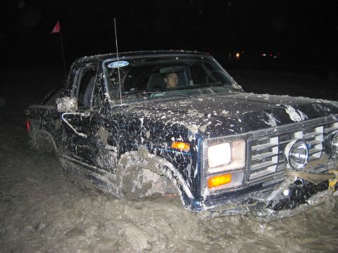 1985 Ford Bronco - This Ford truck appears to be stuck in deep mud, with mud splattered all over its exterior.